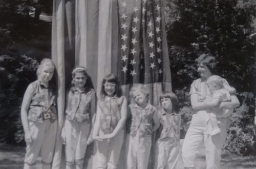 Six little girls and their mother in front of a flag