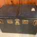 View of the top and front of the travel trunk. Black with gold clasps.